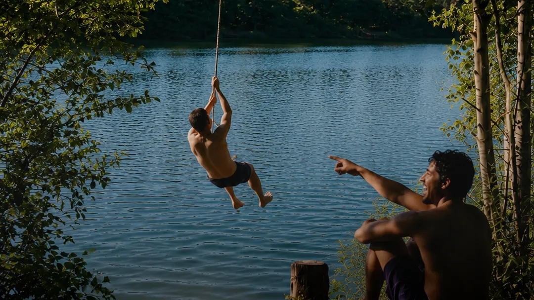 Friend swinging on a rope into a lake while his buddy cheers him on