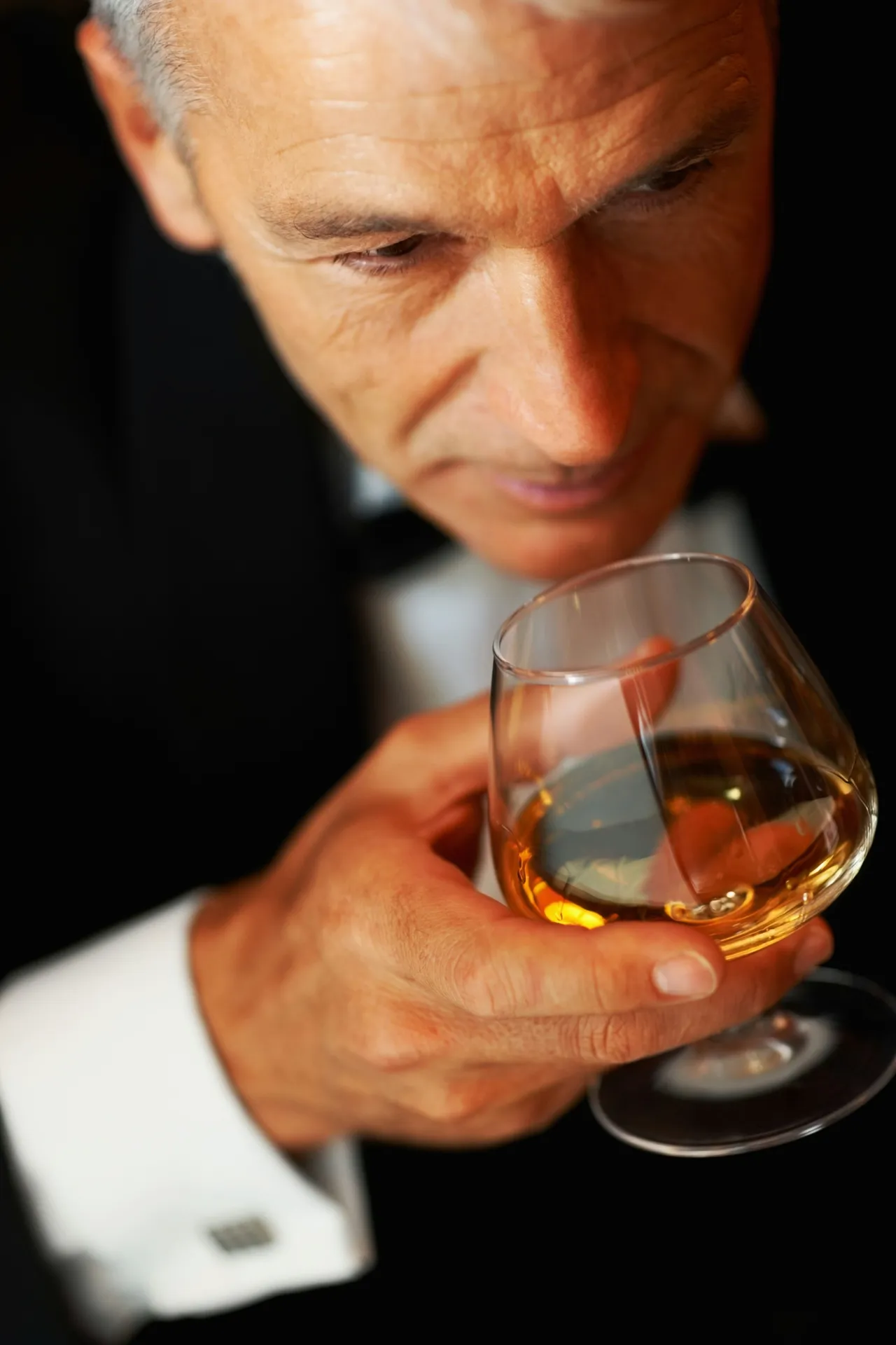 An aged man smelling on a glas of whisky