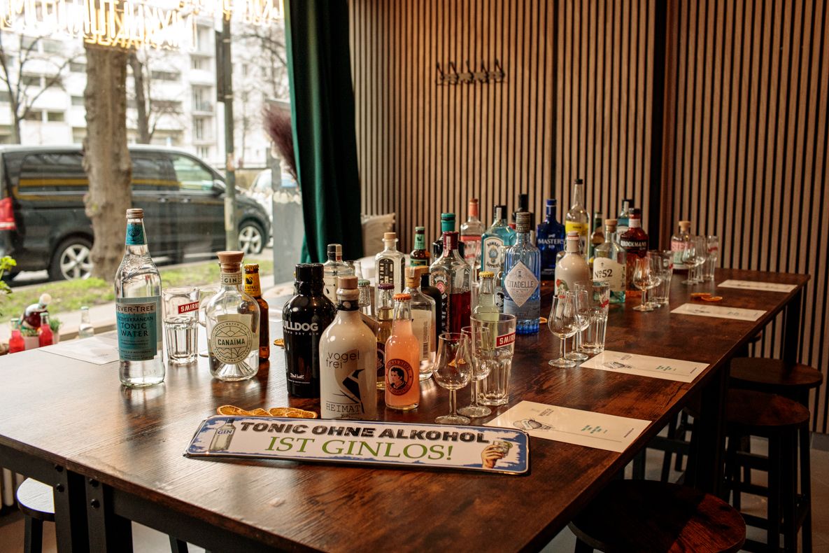 Table lined with an assortment of gin and tonic water bottles, featuring a playful sign reading 'Tonic ohne Alkohol ist ginlos!'