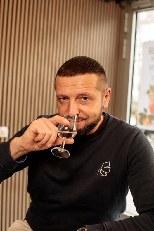 Man sipping gin from a tasting glass while looking toward the camera.