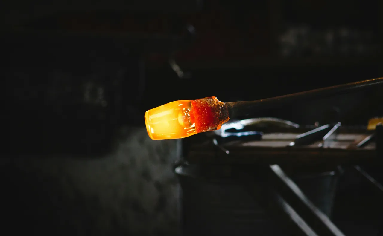 Close-up of a glowing orange molten glass tip on a rod against a dark background