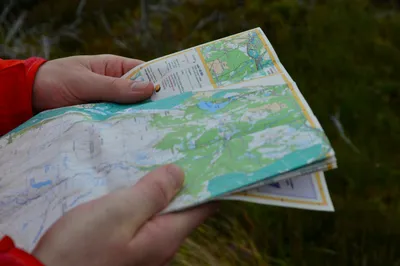 Close-up of hands holding folded topographic maps for an orienteering or GPS treasure hunt activity