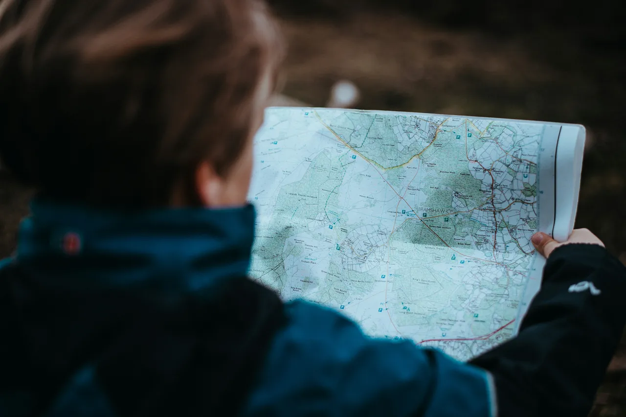 Person in a blue jacket viewed from behind, reading a detailed trail map during an outdoor navigation activity