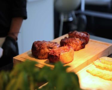 Grilled meat pieces resting on a wooden cutting board under warm light