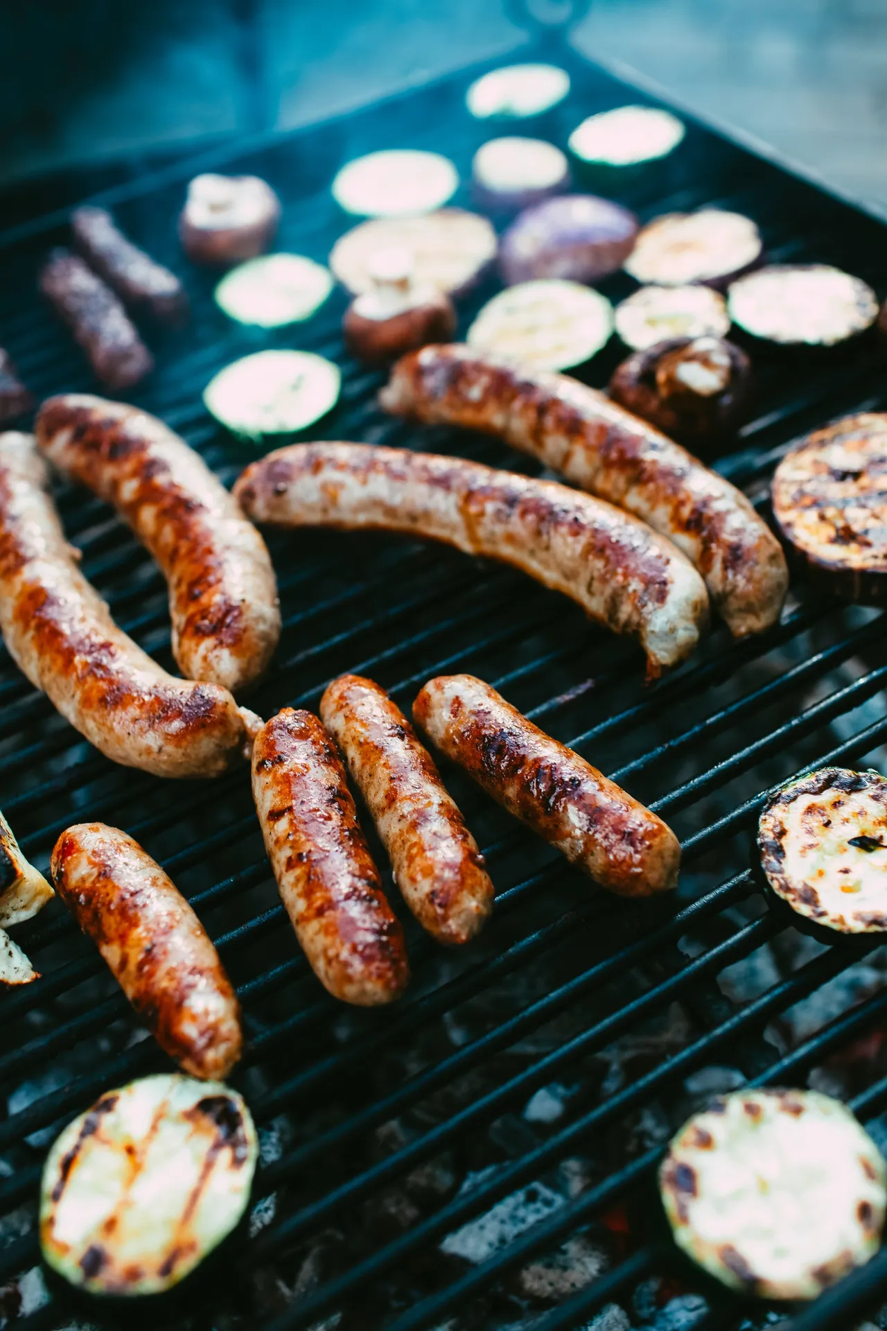 Three grilled sausages are served on a plate over a bed of sauerkraut, garnished with a sprig of fresh rosemary and sweet mustard on the side.