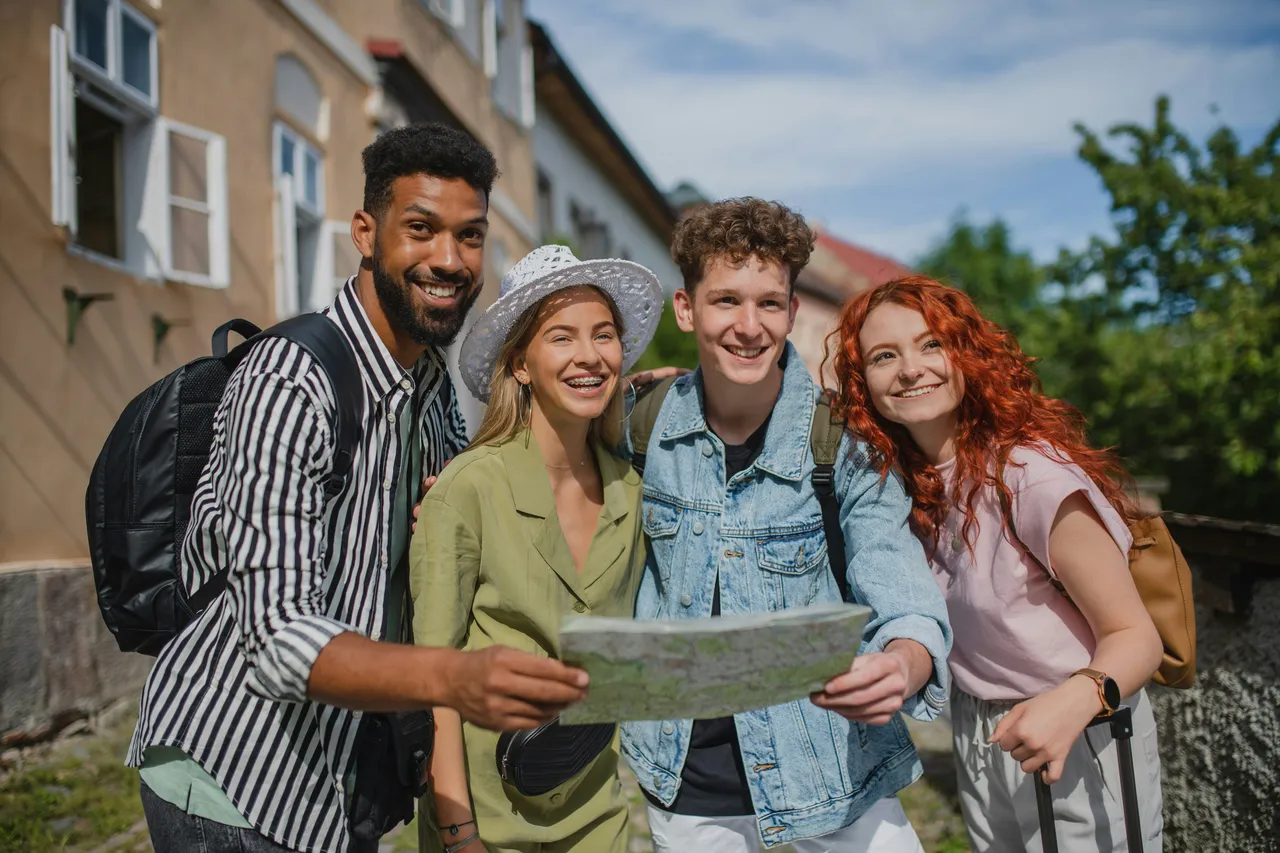 Four smiling friends with backpacks looking at a map together while traveling