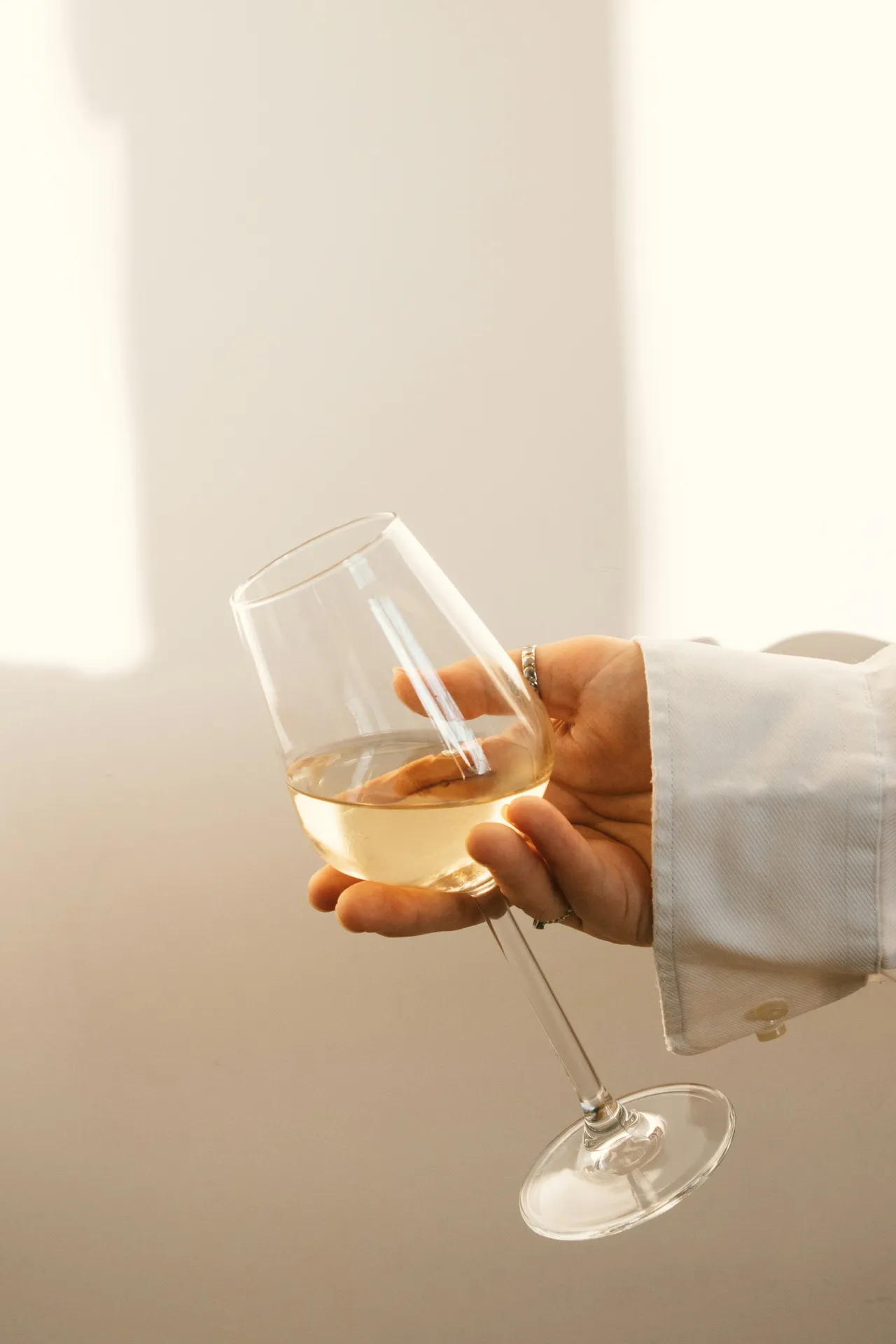 Hand holding a glass of white wine against a light background