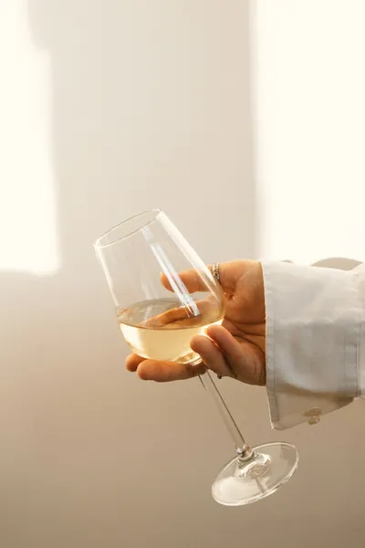 Hand holding a glass of white wine against a light background