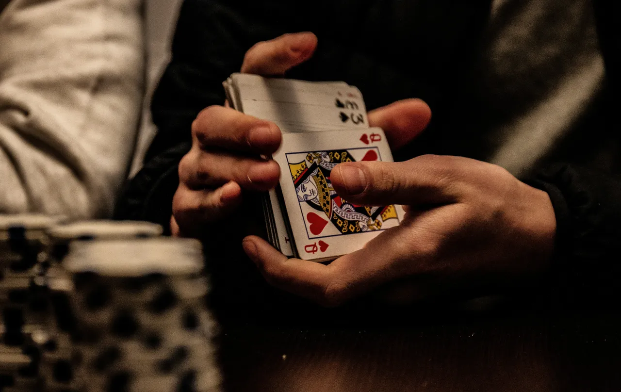 Close-up of hands shuffling a deck of playing cards, queen of hearts visible on top