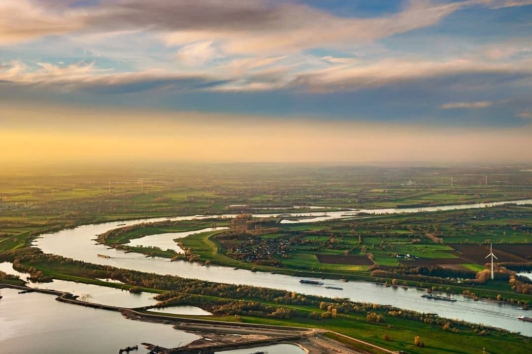 Winding river through a green landscape at sunset, seen from a helicopter