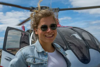 Happy young woman with sunglasses standing in front of a helicopter before take-off