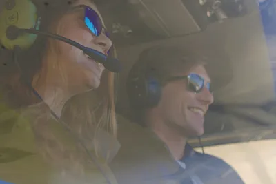 Two smiling passengers wearing headsets and sunglasses enjoying a helicopter flight