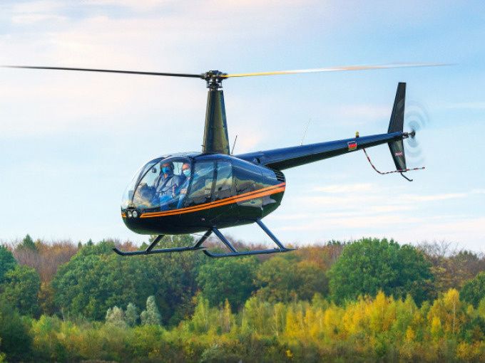 A black and orange helicopter flying in the air with a autumn forest in the background