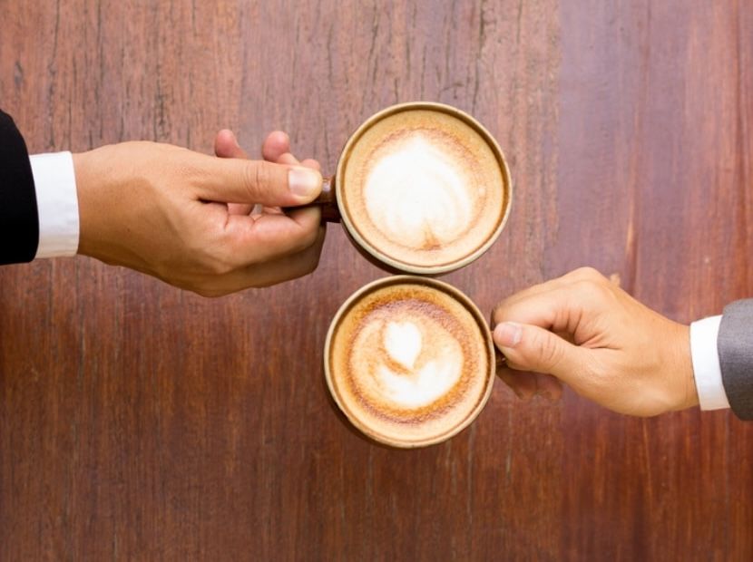 Two people grabbing a coffee cup from a table
