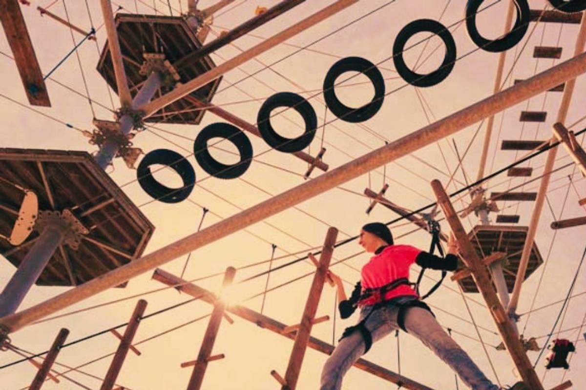 Woman crossing an obstacle in a high ropes course at sunset