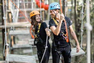 Smiling couple with helmets and harnesses climbing a forest ropes course
