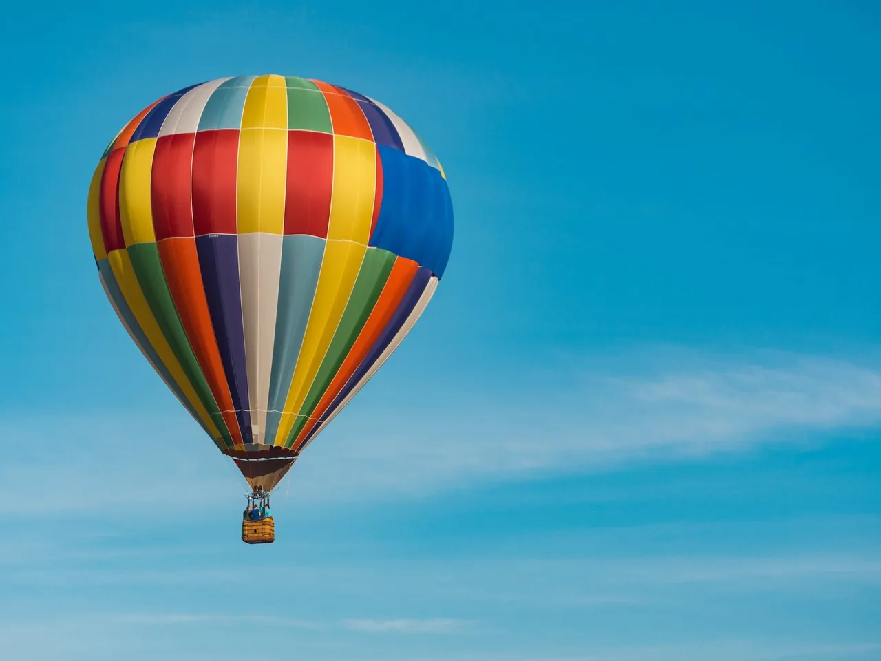 Vibrant multicolored striped hot air balloon floating against a clear blue sky