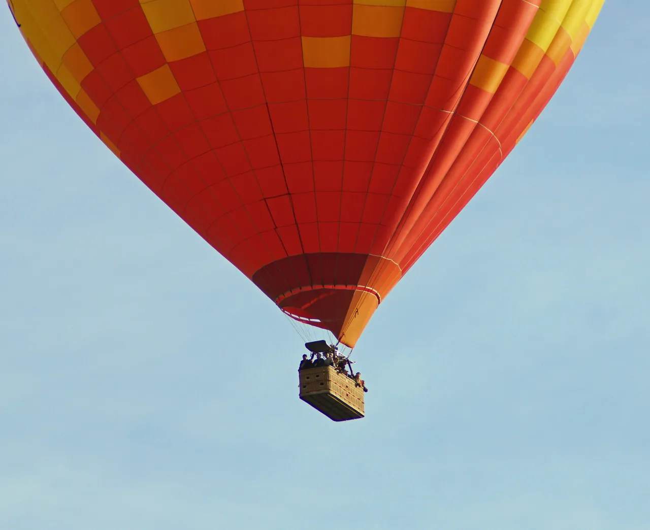 A large hot air balloon resting on a grassy field as ground crew prepare it for deflation.
