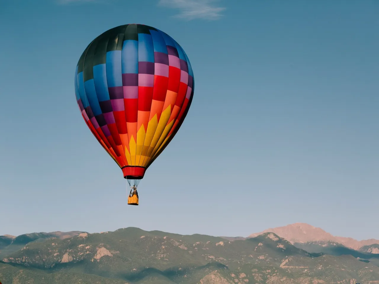 Colorful geometric patterned hot air balloon in red, orange and blue floating above a scenic mountain range
