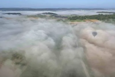 Morning fog filling the valleys between wooded hills, seen from a hot air balloon