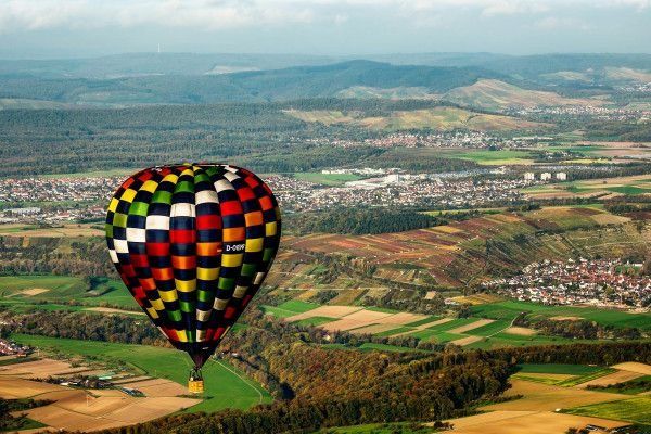 Checkered hot air balloon flying over green hills, fields and villages
