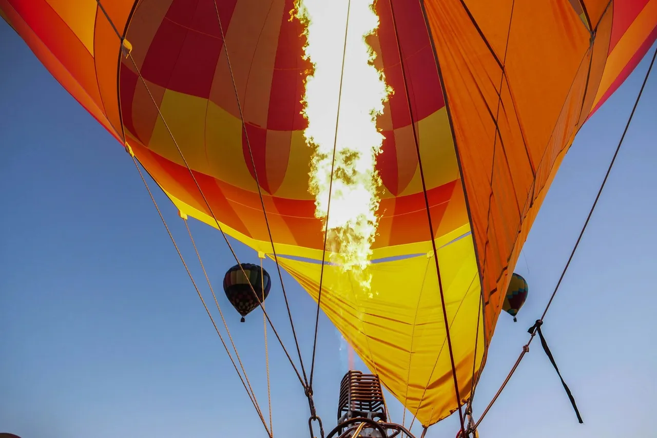 Burner flame heating the air inside a colourful hot air balloon envelope during preparation for take-off