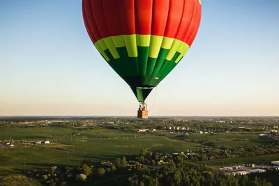 Red, yellow and green hot air balloon drifting over open countryside at sunset