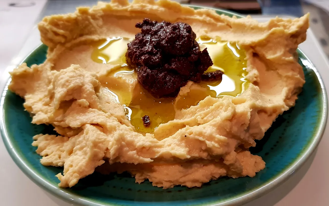 Creamy hummus topped with tapenade on a ceramic plate