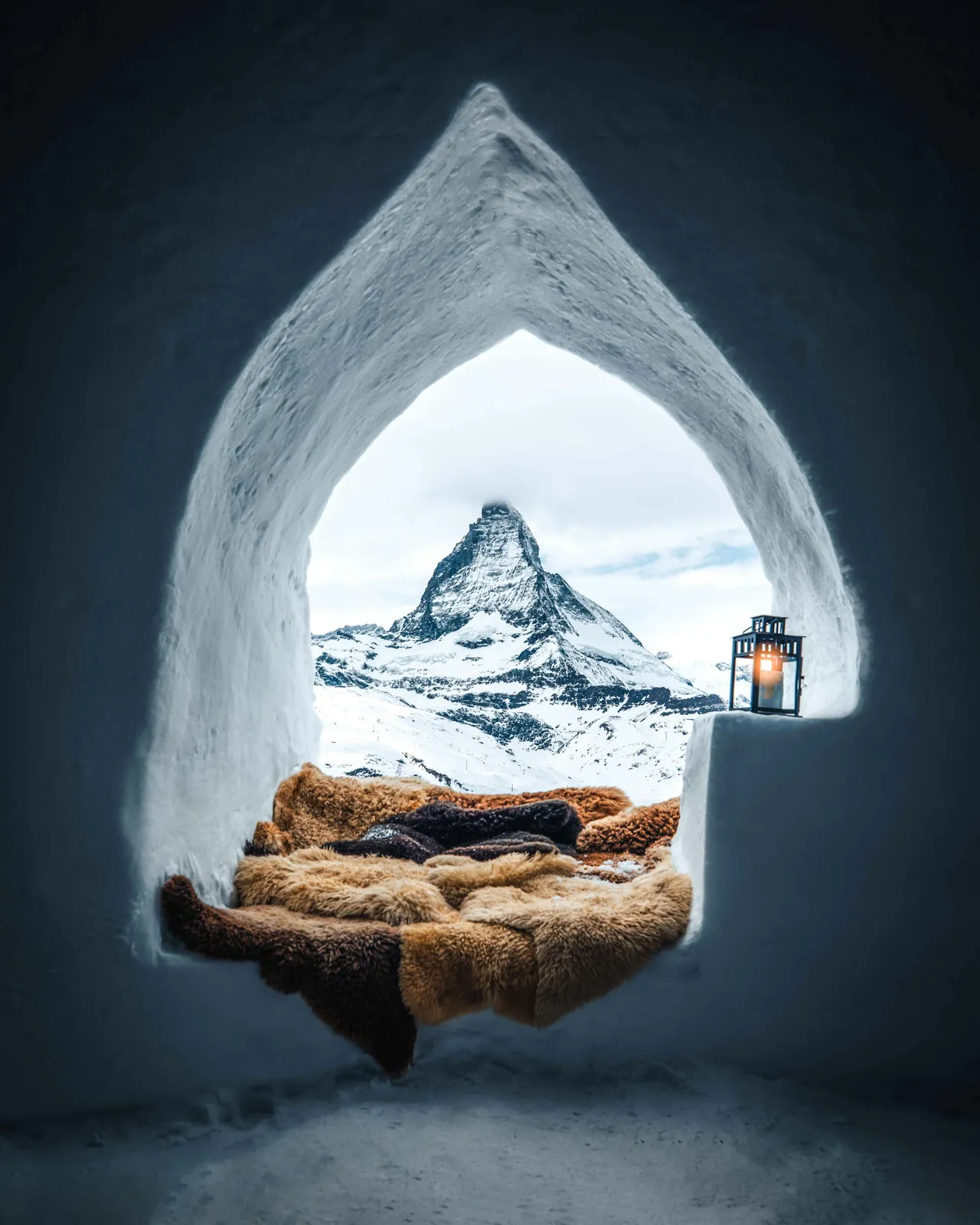 ice building resembling a stylized igloo, surrounded by snow and winter rocks under a white sky.