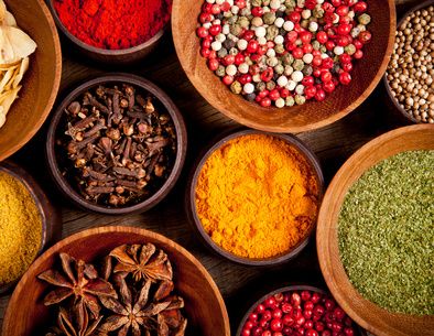 Colourful spices including star anise, cloves, peppercorns and turmeric in wooden bowls