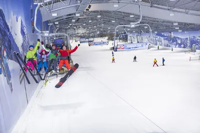 Cheerful skiers and snowboarders riding a four-seater chairlift in an indoor ski hall