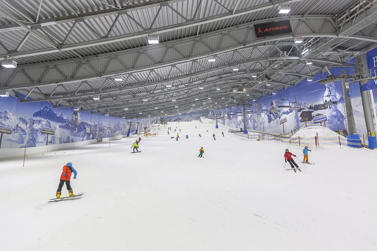 Wide indoor ski slope with skiers and snowboarders on fresh snow