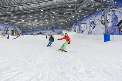 Skier and snowboarder riding side by side on an indoor ski slope
