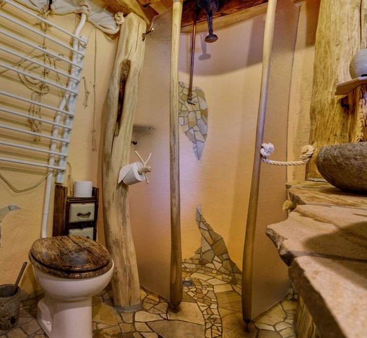 Treehouse bathroom with stone mosaic floor, shower, wooden toilet seat and river stone basin