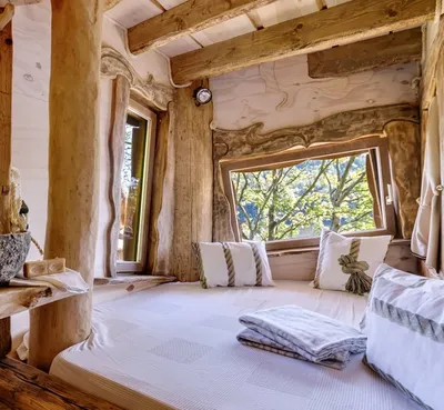 Large bed with white linens beside a panoramic window with treetop views