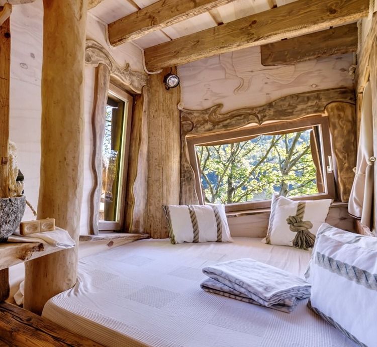 Large bed with white linens beside a panoramic window with treetop views