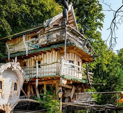 Three-story wooden treehouse with balconies and carved details surrounded by green forest