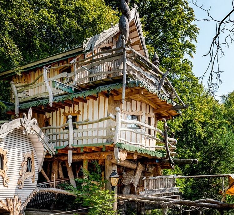 Three-story wooden treehouse with balconies and carved details surrounded by green forest