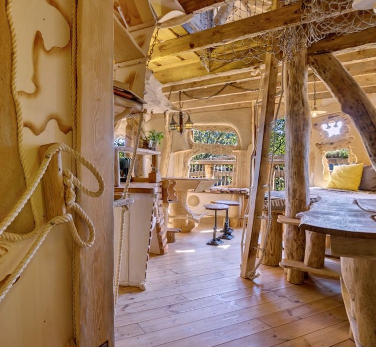 Open-plan living area of a treehouse with tree trunk pillars, rope details and dining table