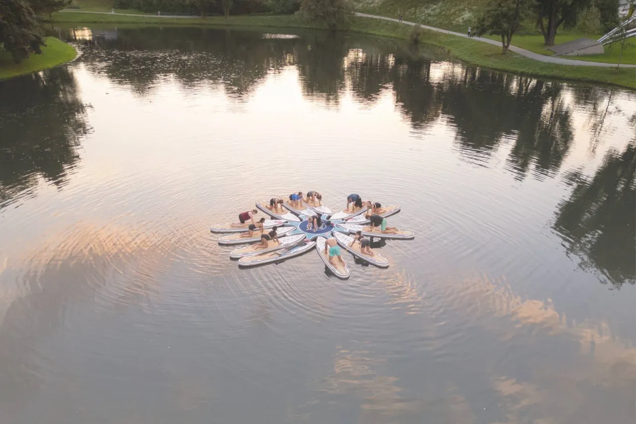 Group doing stand-up paddle yoga on connected boards in the middle of a calm lake
