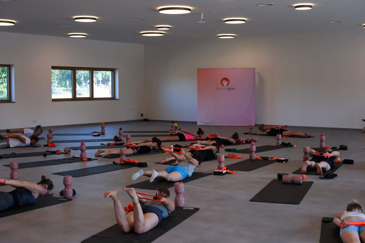 Fitness class doing exercises on mats with foam rollers and resistance bands in a bright studio
