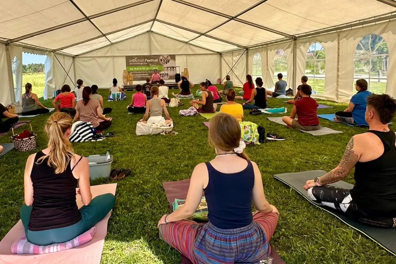 Yoga and meditation class sitting cross-legged on mats in an open tent on the grass