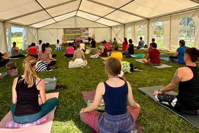 Yoga and meditation class sitting cross-legged on mats in an open tent on the grass