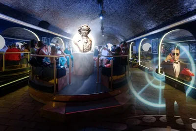 Visitors gathered around a glowing white bust of Beethoven in a brick-vaulted underground exhibit room, with a spy-themed projection nearby