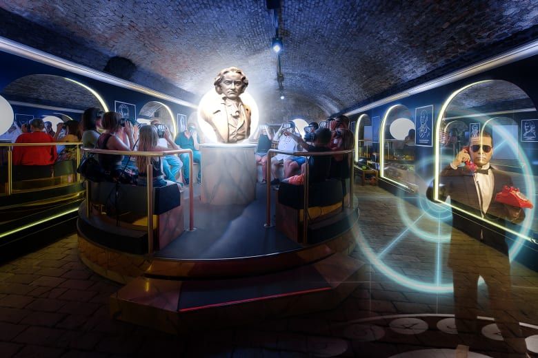 Visitors gathered around a glowing white bust of Beethoven in a brick-vaulted underground exhibit room, with a spy-themed projection nearby