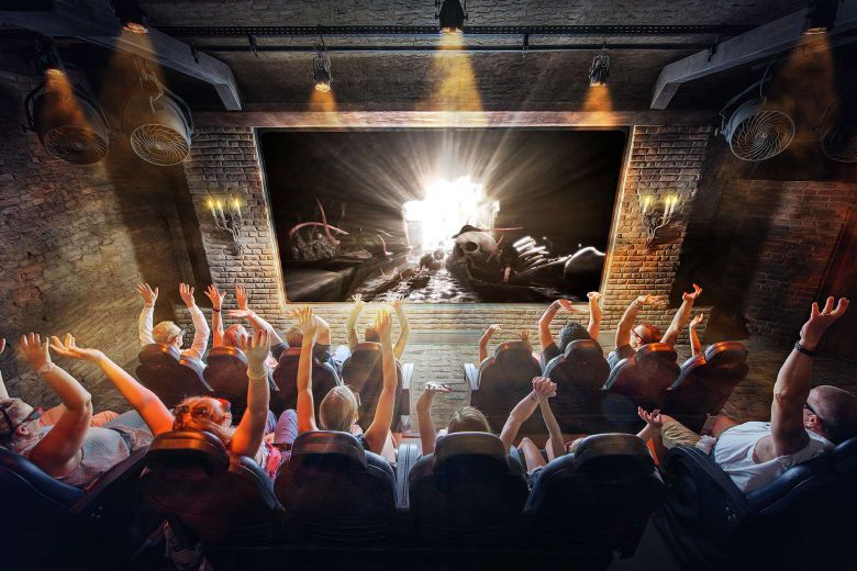 Audience raising their hands in excitement inside a themed 4D cinema during a screening