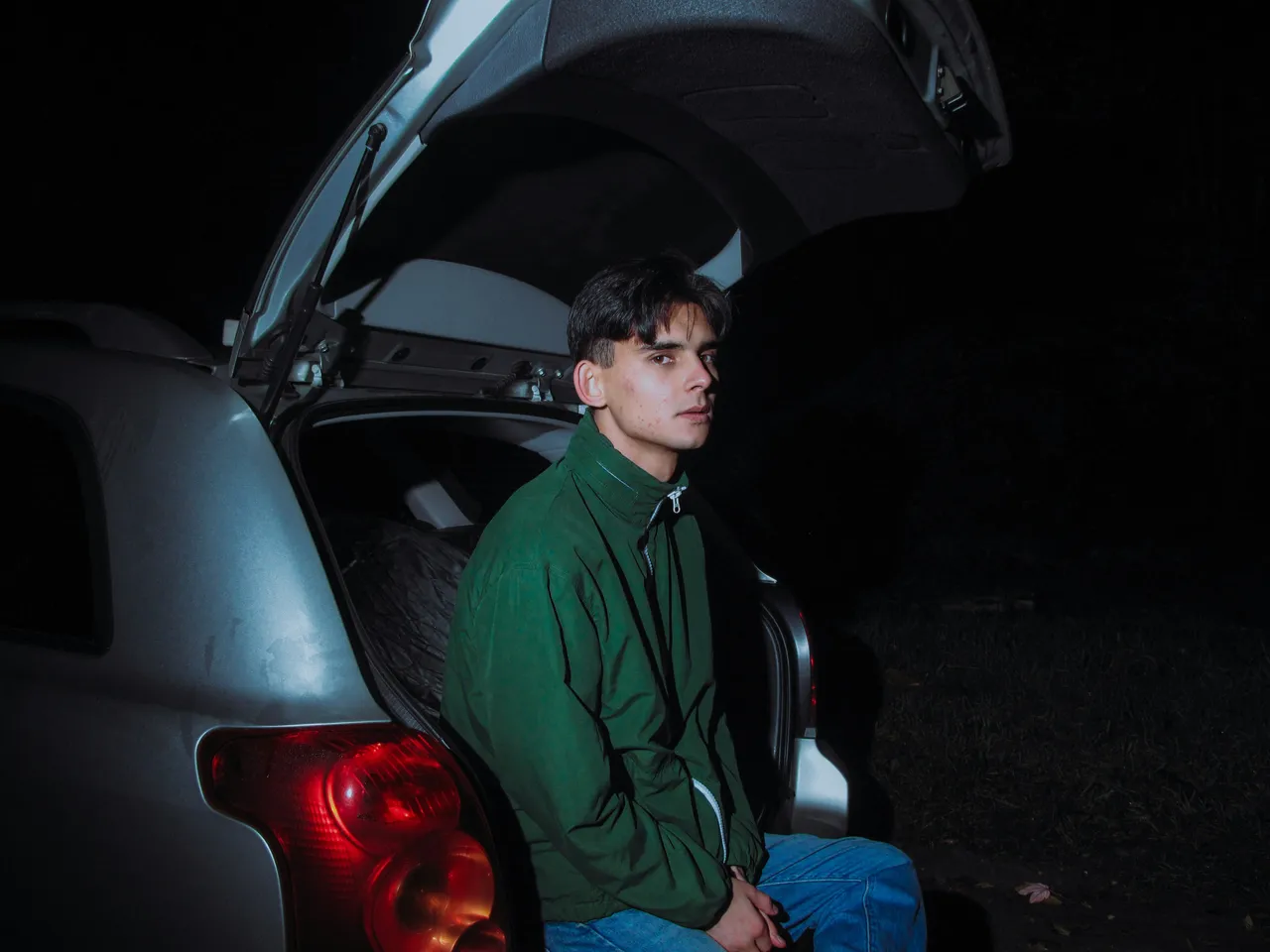 Young man sitting in the open trunk of a car at night