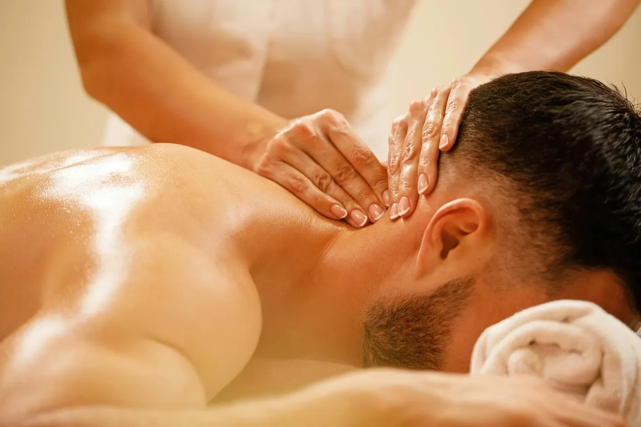 A man lying face down while a massage therapist works on his neck and upper shoulder muscles.