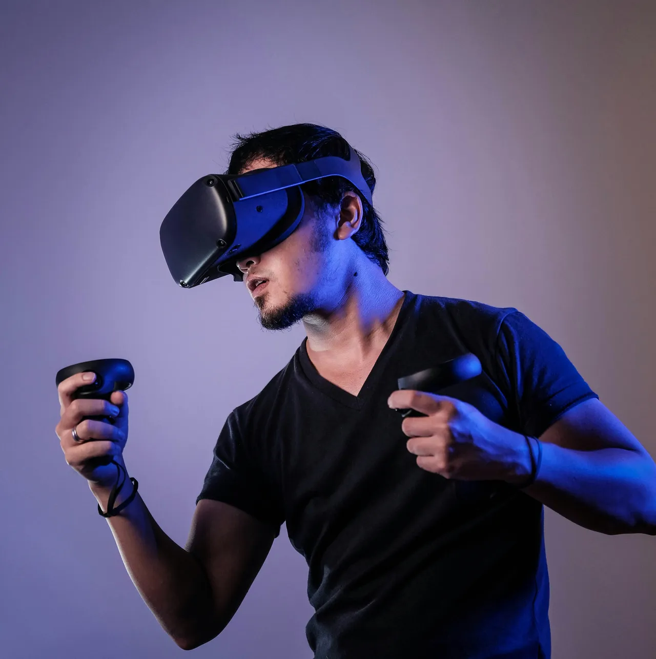 A man wearing a virtual reality headset and holding two motion controllers under dramatic blue lighting.