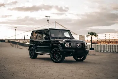 Black Mercedes-AMG G63 with illuminated round headlights by the river